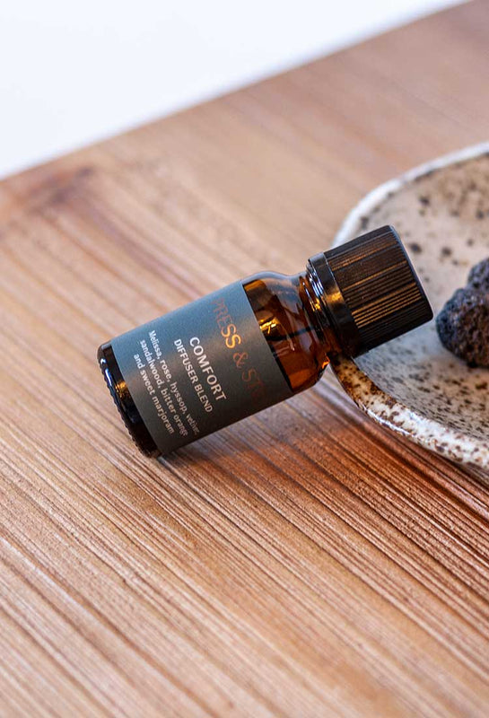 Comfort diffuser blend featuring essential oils of rose, melissa, hyssop, sweet marjoram, bitter orange, vetiver and sandalwood. Set on a speckled dish holding lava diffuser stones.