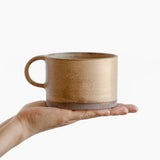 A person holding a Wabi-Sabi stoneware mug with matte glaze in beige and light bottom.