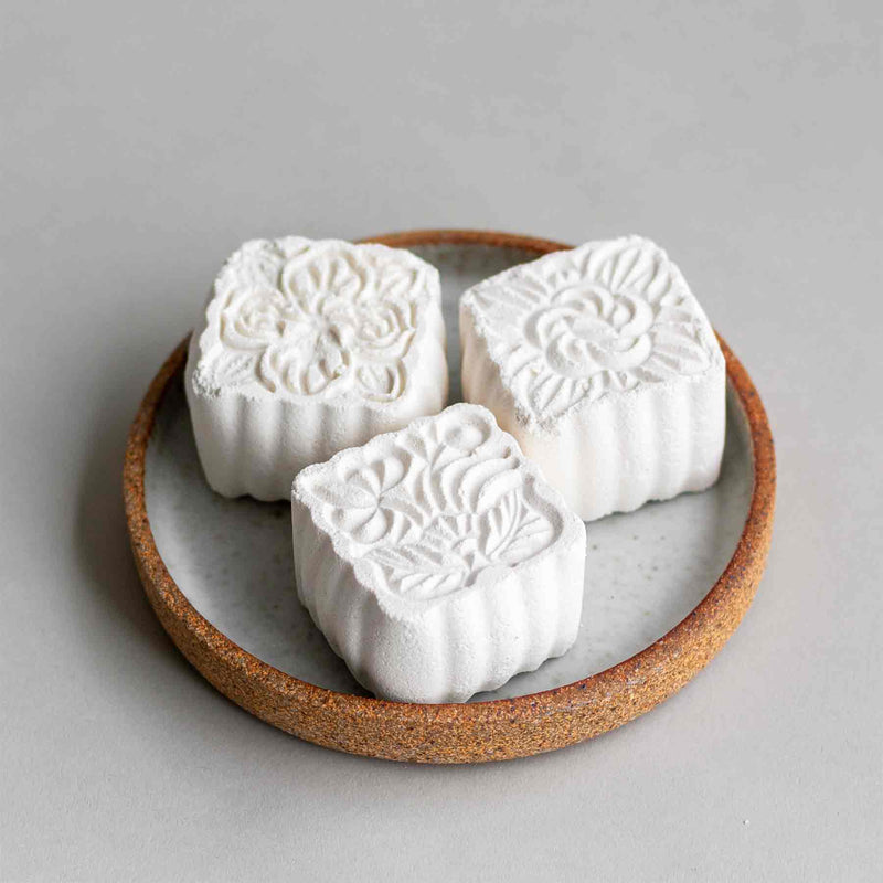 Shower steamers featuring menthol and eucalyptus, pine and lavender essential oils - three tablets on a rustic modern ceramic dish.