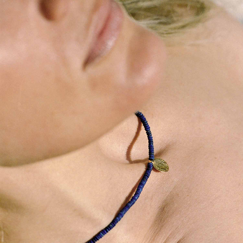 A woman wearing the Relic necklace from TAKARA's Enso collection. This choker necklace is made with lapis beads and a 10k charm in the form of an ancient coin.
