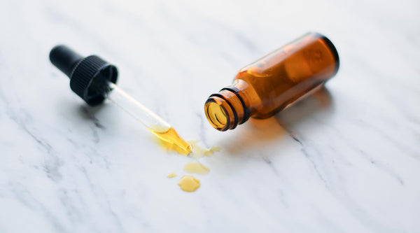 Amber glass bottle with dropper filled with orange-colored retinol. Shown against a marble counter.