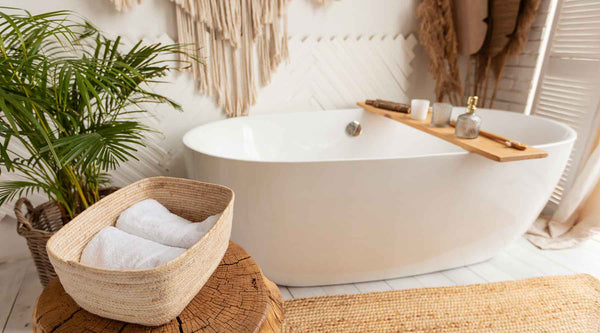 Modern bohemian bathroom with a freestanding white tub, rustic wood stool with towels, and a palm tree.