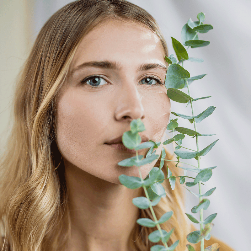 A woman with radiant complexion smelling a fresh eucalyptus branch.