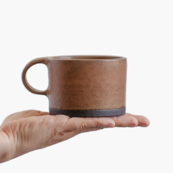 A person holding a Wabi-Sabi stoneware mug with matte glaze in brown.