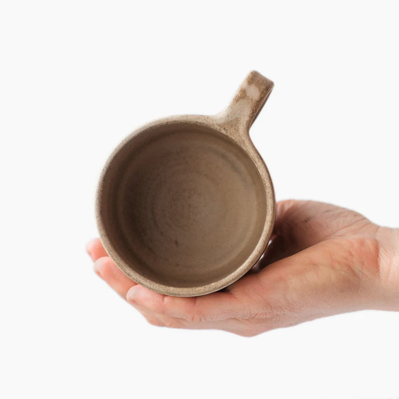 A person holding a slightly smaller beige Wabi-Sabi stoneware mug. View is of the inside of the mug.