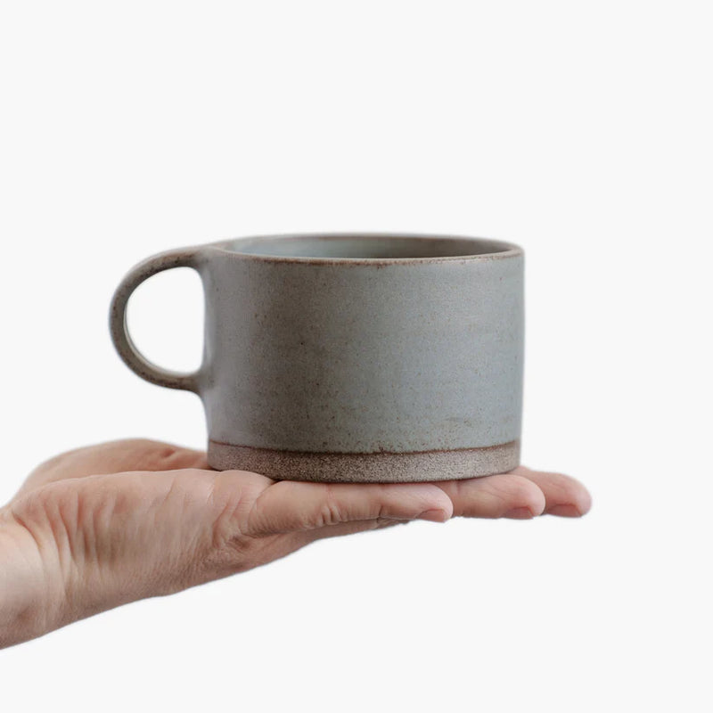 A person holding a Wabi-Sabi stoneware mug with matte glaze in grey-blue.