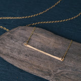 Hammered 14k gold filled pendant on a 16" gold filled chain. Resting on a piece of driftwood against a blue backdrop.