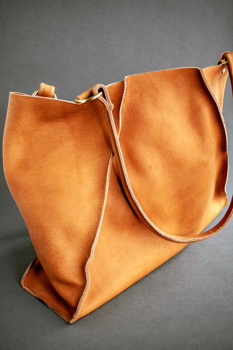 Soft yet sturdy unlined leather tote handmade by J Paige & Co, using leather sourced in the U.S. The asymmetrical seams make this tote unique. The camel color is quite striking against the dark grey backdrop.