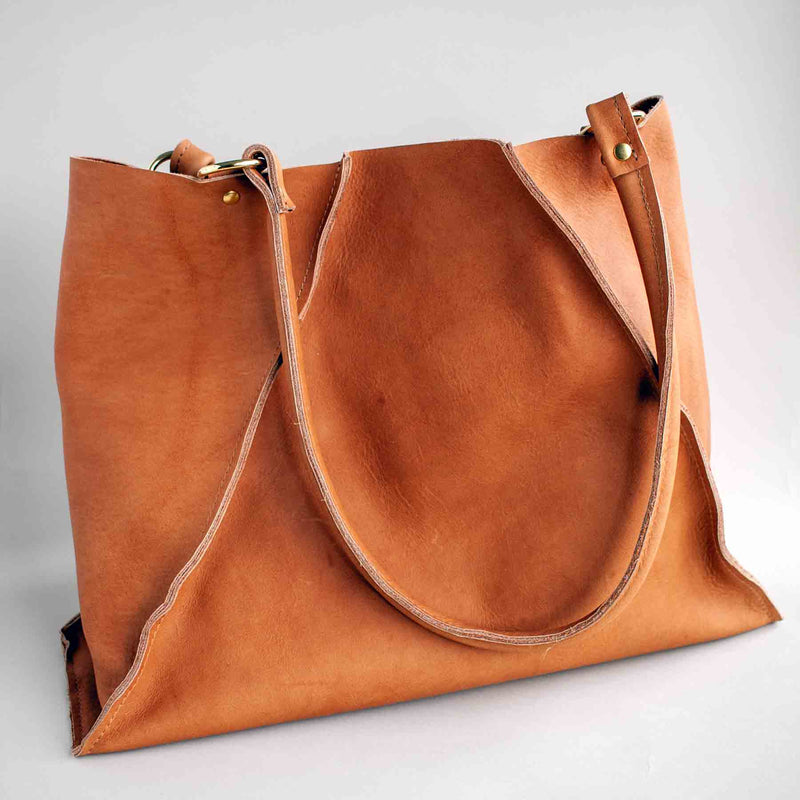 Soft yet sturdy unlined leather tote handmade by J Paige & Co, using leather sourced in the U.S. The asymmetrical seams make this tote unique. Shown against a light grey backdrop.