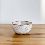 Small ceramic dish in speckled glaze by Lala's Fresh Pots. Resting on a hickory board, against a white backdrop.