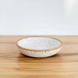 Medium ceramic dish in speckled glaze by Lala's Fresh Pots. Resting on a hickory board, against a white backdrop.