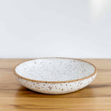 Large ceramic dish in speckled glaze by Lala's Fresh Pots. Resting on a hickory board, against a white backdrop.