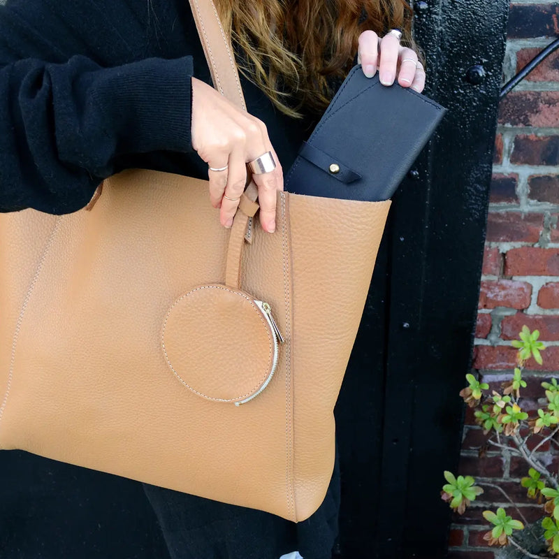 The sleek, minimal yet oh-so-functional Maxi wallet by Shana Luther. Made with vegetable-tanned leather and solid brass stud hardward. Shown here: a woman putting the black Maxi wallet in her oak-colored June tote.