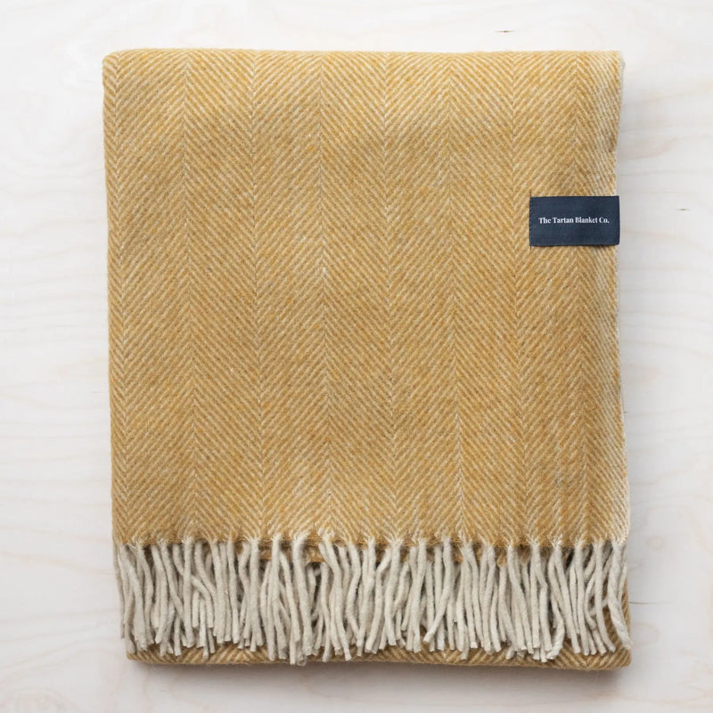 A neatly folded recycled wool mustard-colored herringbone blanket with fringe by The Tartan Blanket Co.