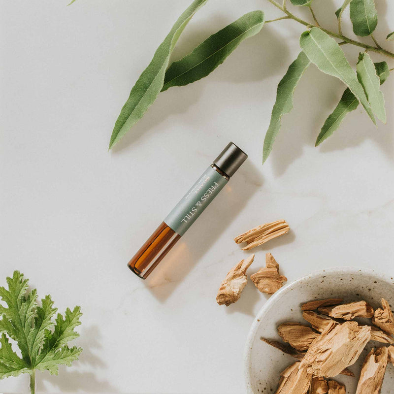 Press & Still Balance essential oil blend next to sandalwood chips, and eucalyptus and geranium leaves.