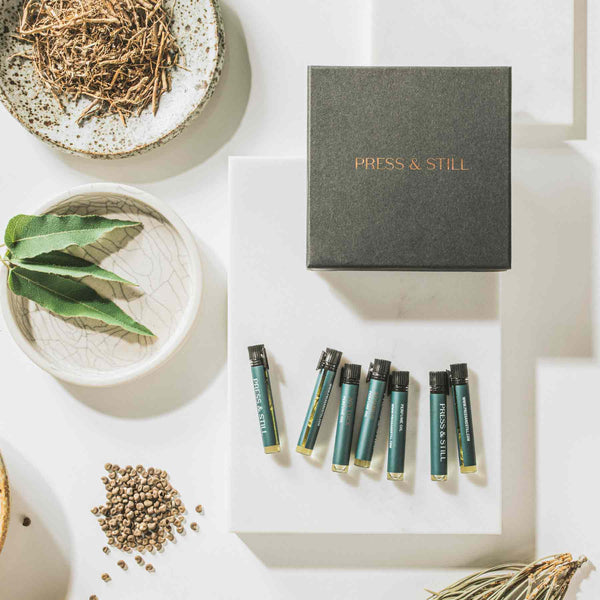Vials of botanical perfume next to the discovery set box, eucalyptus leaves, vetiver and coriander seeds.