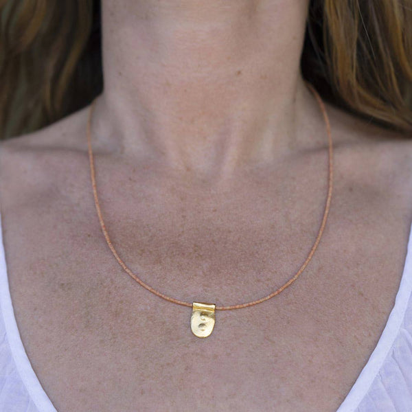 Woman wearing the coral bead and 10k charm Mystic necklace by TAKARA.