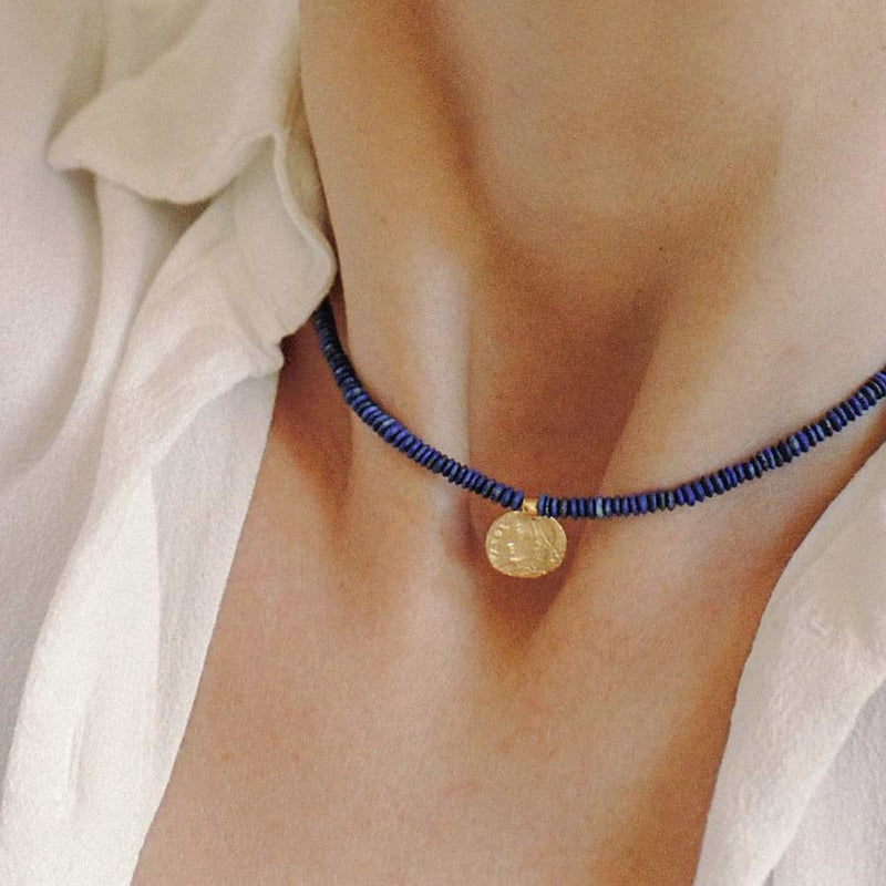 A woman wearing the Relic necklace necklace made with lapis beads and a 10k yellow gold charm shaped from an ancient coin.