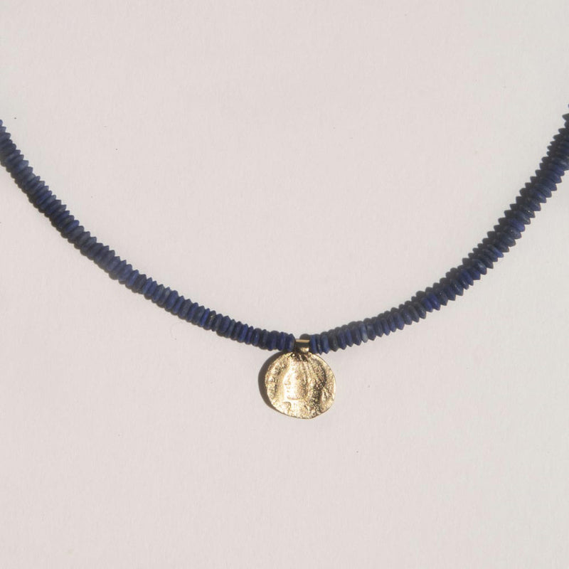 Close-up of the Relic necklace made with lapis beads and a 10k yellow gold charm shaped from an ancient coin.