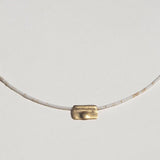 A close-up of the 10k yellow gold token pendant on cream- and coral-colored stone beads.